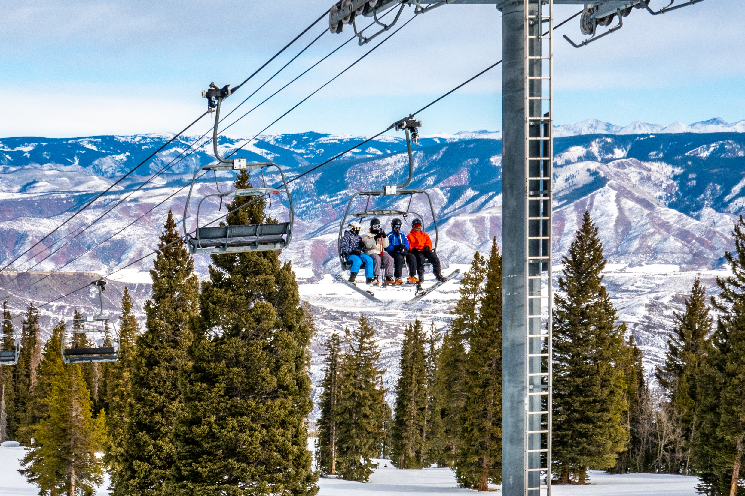Skiers and snowboarders ascend the Alpine Springs chairlift at the Aspen Snowmass ski resort, in the Rocky Mountains of Colorado on a partly cloudy winter day.
